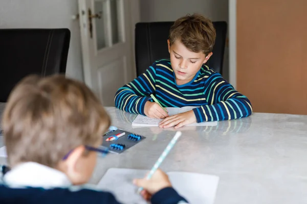 コロナからの隔離期間中に宿題をしている2人の勤勉な学校の少年とコビン19パンデミックの病気 子供たち ペンで書く兄弟 家にいる 家庭教育の概念 — ストック写真