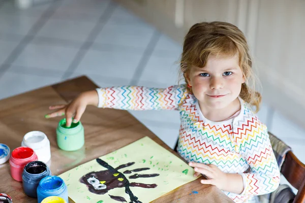 Little creative toddler girl painting with finger colors an owl bird. Active child having fun with drawing at home, in kindergaten or preschool. Games, education and distance learning for kids.