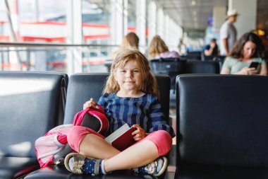 Küçük kız havaalanında büyük pencerede biniş için bekliyor. Pasaportu olan sevimli bir çocuk yaz tatiline gitmeyi dört gözle bekliyor..