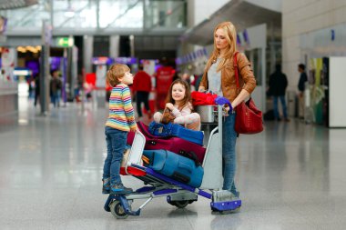 İki küçük çocuk, erkek ve kız, kardeşler ve anne havaalanında. Çocuklar, aile seyahati, uçakla tatile gitmek ve bir kadının terminalden uçmak için ittiği valizlerle tramvayda beklemek.