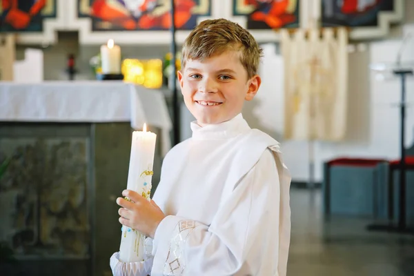 小男孩接受他的第一次圣餐 快乐的孩子拿着洗礼蜡烛 天主教的诅咒的传统 在祭坛附近的教堂里穿着白色传统礼服的孩子 — 图库照片