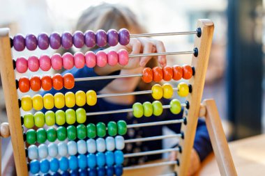 Küçük anaokulu kızı eğitici tahta gökkuşağı oyuncak tezgahı abaktüsüyle oynuyor. Gözlüklü sağlıklı mutlu çocuk, güneşli bir günde evde saymayı ve renkleri öğreniyor.