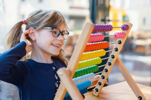 学龄前小女孩玩教育木制彩虹玩具柜台算盘 健康快乐的孩子 戴着眼镜 学习计数和色彩 在阳光灿烂的日子里呆在室内 — 图库照片