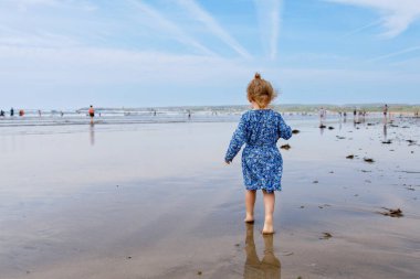 Little cute toddler girl at the Ballybunion surfer beach, having fun on with playing on west coast of Ireland. Happy child enjoying Irish summer and sunny day with family