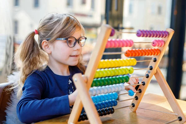 学龄前小女孩玩教育木制彩虹玩具柜台算盘 健康快乐的孩子 戴着眼镜 学习计数和色彩 在阳光灿烂的日子里呆在室内 — 图库照片
