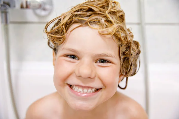 Cute child with shampoo foam and bubbles on hair taking bath. Portrait of happy smiling preschool girl health care and hygiene concept. Washes hair by herself