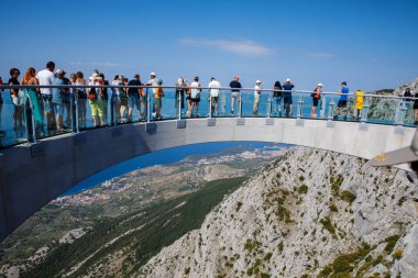 BIOKOVO, Hırvatistan - 17 Ağustos 2022: Biokovo dağında yeni inşa edilen gökyüzünde yürüyen turistler. Girişten, kasabalardan ve denizden geniş görüş alanı var..