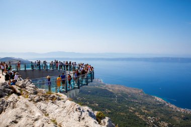 BIOKOVO, Hırvatistan - 17 Ağustos 2022: Biokovo dağında yeni inşa edilen gökyüzünde yürüyen turistler. Girişten, kasabalardan ve denizden geniş görüş alanı var..