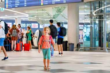 Havaalanı terminalindeki küçük anaokulu kızı. Mutlu çocuk uçakla tatile çıkıyor. Pasaportu ve çantası olan gülümseyen çocuk.