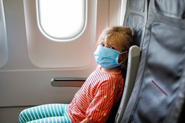 Cerrahi maskeli küçük bir kız uçakla seyahat ederken korunuyor. Coronavirus ve gribe karşı koruma.