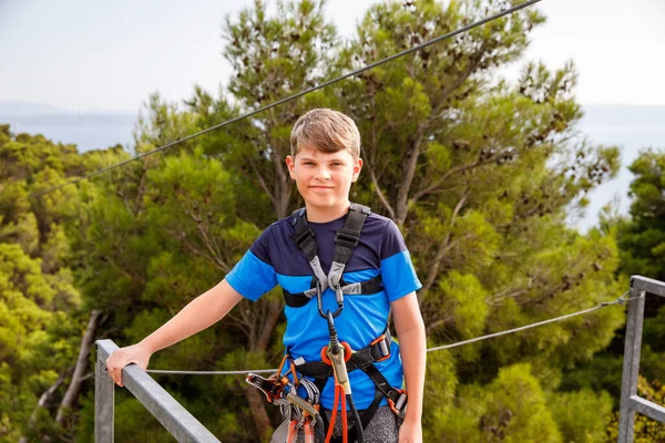 ジップラインアドベンチャーの準備をしている学校の少年 幸せな活動的な子供は頭部に安全ヘルメットを置いた 山に登る夏の楽しみ — ストック写真