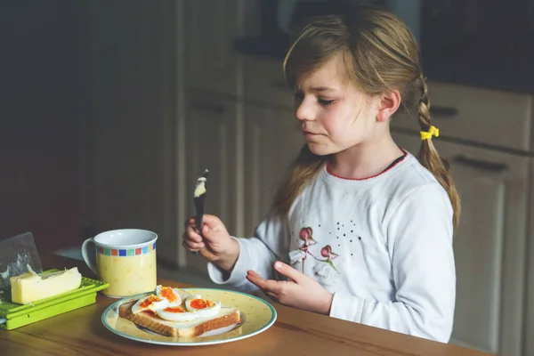 Little smiling girl have a breakfast at home. Preschool child eating sandwich with boiled eggs. Happy children, healthy food and meal