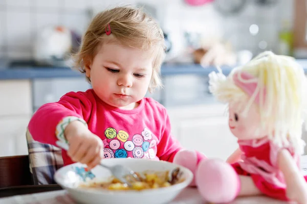 Adorable baby girl eating from fork vegetables and pasta. food, child, feeding and development concept. Cute toddler, daughter with spoon sitting in highchair and learning to eat by itself