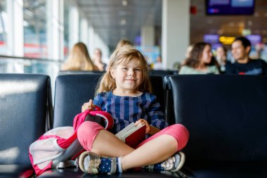 Küçük kız havaalanında büyük pencerede biniş için bekliyor. Pasaportu olan sevimli bir çocuk yaz tatiline gitmeyi dört gözle bekliyor..