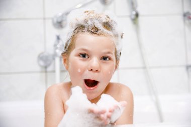 Şampuan köpüğü ve banyo yapan saçlarında kabarcıklar olan tatlı bir çocuk. Gülümseyen anaokulu kızı sağlık hizmetleri ve hijyen konseptinin portresi. Saçlarını kendi yıkar.