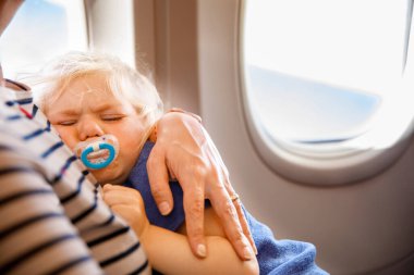 Küçük çocukla uçakla seyahat eden bir kadın. Üzgün, yeni yürümeye başlayan kız annesiyle birlikte uçak penceresinde oturuyor. Annelik kavramı. Ağlayan bebek
