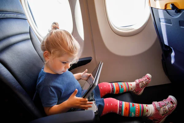 小孩子的小女孩坐飞机旅行 快乐的小孩坐在飞机窗边 在飞行过程中使用数字平板电脑 带着孩子出国旅行 — 图库照片
