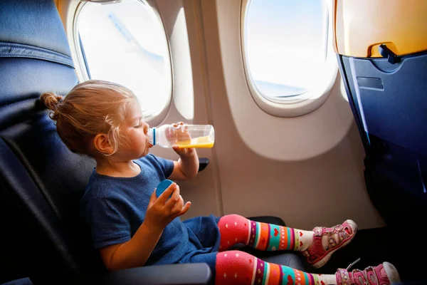可爱的小女孩坐飞机旅行 蹒跚学步的小孩坐在飞机窗前喝橙汁 和孩子们一起出国旅行暑假的家庭 — 图库照片