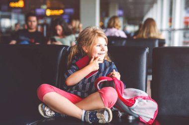 Küçük kız havaalanında büyük pencerede biniş için bekliyor. Pasaportu olan sevimli bir çocuk yaz tatiline gitmeyi dört gözle bekliyor..