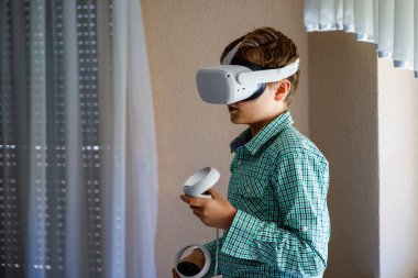 Genç çocuk evde sanal gerçeklik kasklarıyla VR oyunları oynuyor. Heyecanlı ergen çocuk kontrolörleri tut ve başka yere bak. Video oyunları oynayan VR kasklı bir genç