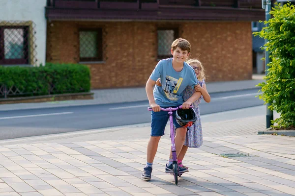 就学前の女の子と市内のスクーターに乗る学校の少年 妹と子供の弟はローラーに乗る 子供たちはスクーターで屋外で遊ぶ 子供のためのアクティブなレジャーや屋外スポーツ — ストック写真
