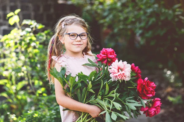 赤とピンクの牡丹の花の巨大な花束を持つかわいい愛らしい小さな就学前の女の子 暖かい春や夏の日に家庭菜園で笑顔の就学前の子供の肖像画 — ストック写真