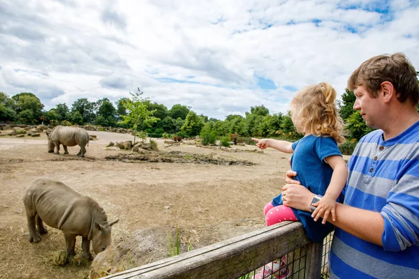 かわいいかわいい幼児の女の子と父親は動物園で野生のサイを見ています 幸せな赤ちゃんの子供 娘とお父さん 暖かい夏の日に動物サファリパークと一緒に楽しんでいる家族 アイルランド — ストック写真