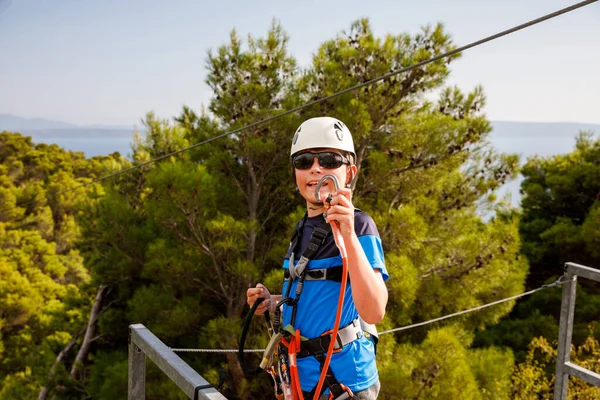 School boy preparing for zipline adventure. Happy active child put safety helmet on head. Summer fun with climbing in mountains