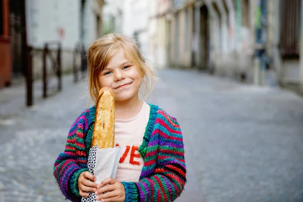 街の通り側に新鮮なフランスのバゲットと愛らしい小さな就学前の女の子 フランスの幸せな小さな子供 — ストック写真