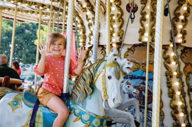 Mutlu pozitif anaokulu kızı St. Malo Fransa 'daki eski klasik atlıkarıncaya biniyor. At üstünde gülümseyen çocuk