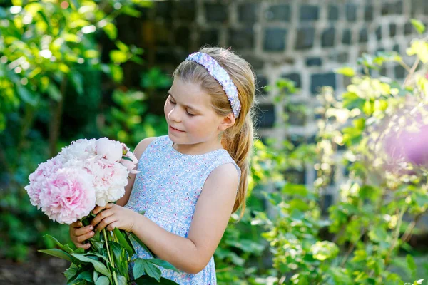 ピンクの牡丹の花の巨大な花束を持つかわいい愛らしい小さな就学前の女の子 暖かい春や夏の日に家庭菜園で笑顔の就学前の子供の肖像画 — ストック写真