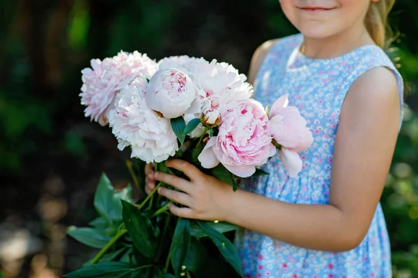 stock image Cute adorable little preschool girl with huge bouquet of blossoming pink peony flowers. Portrait of smiling preschool child in domestic garden on warm spring or summer day. Summertime