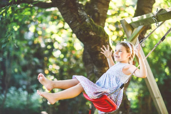 快乐的学龄前小女孩在自家花园荡秋千玩得很开心 在阳光灿烂的春天 可爱的孩子在盛开的树下荡秋千 小孩又笑又哭 — 图库照片
