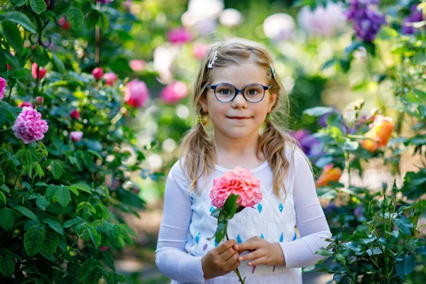 可愛いかわいい就学前の女の子は庭で花とプリンセスドレスをバラ 暖かい春や夏の日に家庭菜園で笑顔の就学前の子供の肖像画 — ストック写真