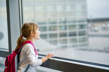 Küçük kız havaalanında Büyük Pencere 'de pansiyon bekliyor. Şirin Çocuk Pencere 'de, uçakların arka planına karşı duruyor. Aile Yaz tatili için ayrılmayı dört gözle bekliyorum..
