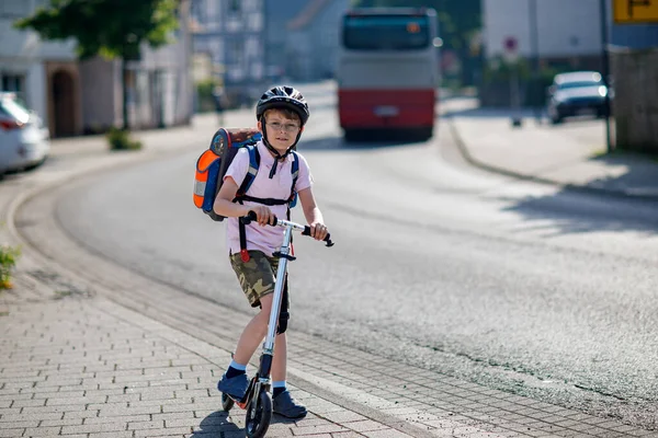 晴れた日にバックパックで市内の彼のスクーターに乗って安全ヘルメットに眼鏡を持つアクティブな学校の少年 学校に行く途中で幸せな子供の自転車 学校への屋外の子供のための安全な方法 — ストック写真