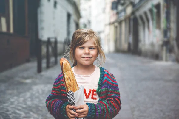 街の通り側に新鮮なフランスのバゲットと愛らしい小さな就学前の女の子 フランスの幸せな小さな子供 — ストック写真