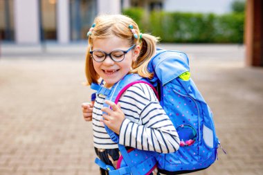 Okuldaki ilk gününde çok tatlı bir kız. Anaokuluna ve anaokuluna yürüyen sağlıklı, güzel bir çocuk. Gözlüklü, gözlüklü mutlu çocuk. Sırt çantası şehir sokaklarında, dışarıda.