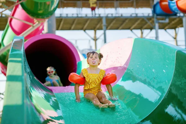 Little preschool girl on water slide in aqua park. Happy child having fun on water slides on family summer vacation in tropical resort. Amusement park with wet playground for young child and baby
