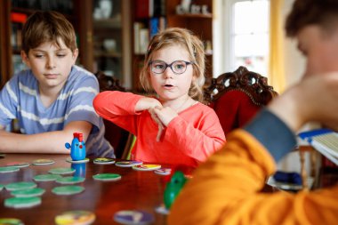 Aile evde masa oyunu oynuyor. Çocuklar stratejik oyunlar oynar. Küçük kız kardeş ve iki erkek kardeş. Kapalı alanda eğlenceli aktiviteler. Kardeşler arası bağ. Eğitici oyuncaklar