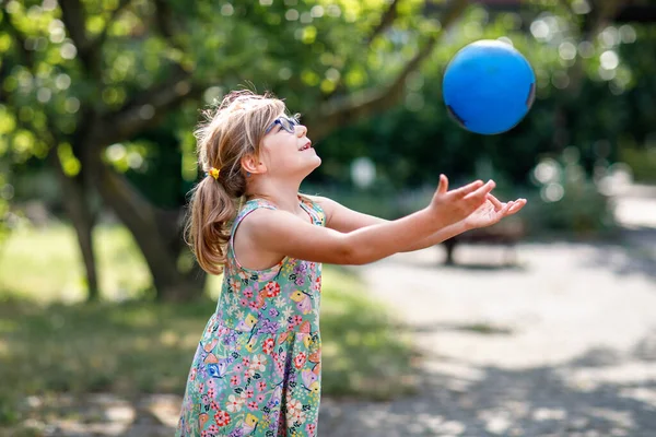 stock image Little preschool girl with eyeglasses playing with ball outdoors. Happy smiling child catching and throwing, laughing and making sports. Active leisure with children and kids. Summer day on backyard.