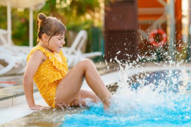 Gün batımında dışarıda yüzme havuzunda oynayan küçük bir anaokulu kızı. Çocuk havuzda yüzmeyi, su sıçratmayı, eğlenmeyi öğreniyor. Aile tatilleri. Sağlıklı çocuklar spor aktivitesi.