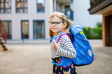 Okuldaki ilk gününde çok tatlı bir kız. Anaokuluna ve anaokuluna yürüyen sağlıklı, güzel bir çocuk. Gözlüklü, gözlüklü mutlu çocuk. Sırt çantası şehir sokaklarında, dışarıda.