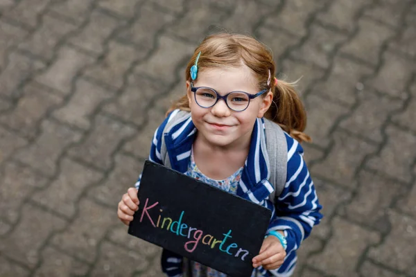 快乐的小女孩手里拿着黑板站在那里 幼儿园的最后一天是德语 在绿地公园 健康的学龄前儿童在户外戴着眼镜 — 图库照片