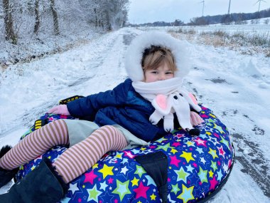 Active prechool girl sliding down the hill on snow tube. Cute little happy child having fun outdoors in winter on sledge . Healthy excited kid tubing snowy downhill, family winter time