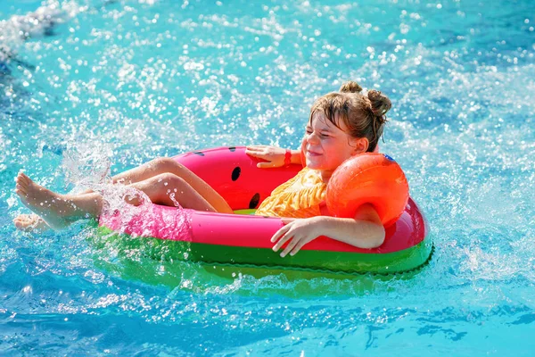 Happy little girl with inflatable toy ring float in swimming pool. Little preschool child learning to swim and dive in outdoor pool of hotel resort. Healthy sport activity and fun for children
