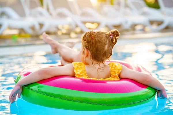 Happy little girl with inflatable toy ring float in swimming pool. Little preschool child learning to swim and dive in outdoor pool of hotel resort. Healthy sport activity and fun for children