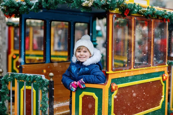 Little preschool girl on a carousel train at Christmas funfair or market, outdoors. Happy child having fun. Traditional xmas market in Germany, Europe. Holiday, children, lifestyle concept.