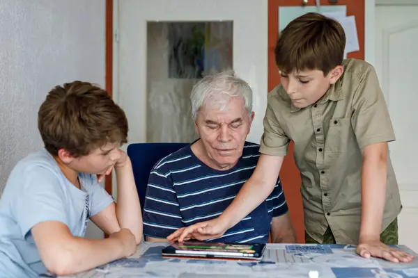 Two Preteen Boys Teaching Grandfather How to Use Internet Safely. Teenage Brothers, School Children with Digital Tablet Playing with Granddad, Senior Man at Home