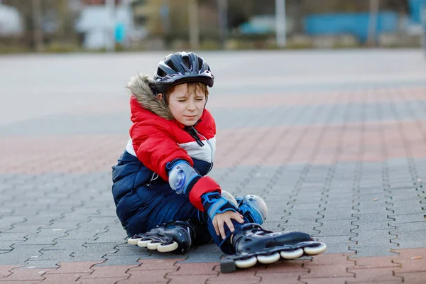 Küçük okul çocuğu şehirde patencilerle kayıyor. Koruyucu giysili çocuk. Aktif okul çocuğu spor yapıyor ve paten kaymayı öğreniyor. Düşmek ve yaralanmak..